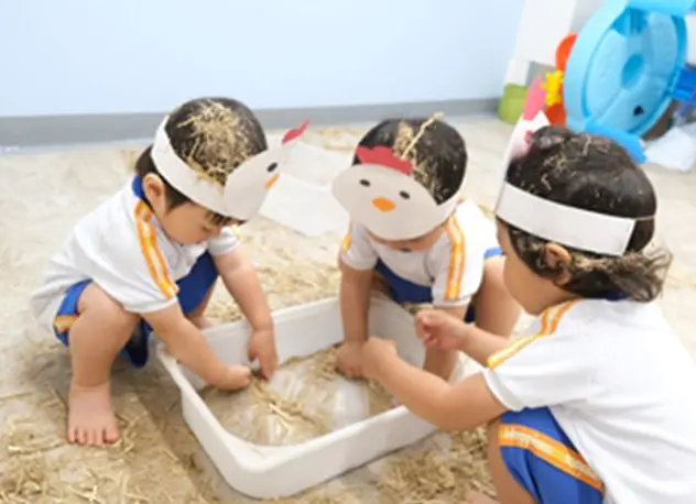 ニワトリの帽子をかぶって藁遊びを楽しむ子どもたち
