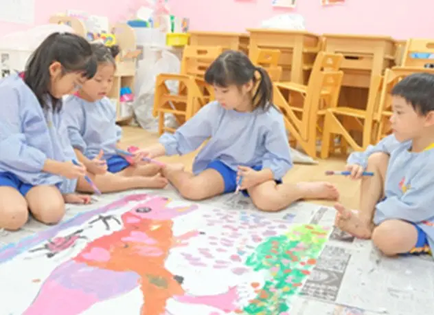 床に広げた大きな絵に色を塗る子どもたち