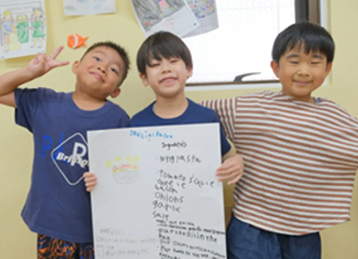 英語で書いたボードを笑顔で持つ3人の子どもたち